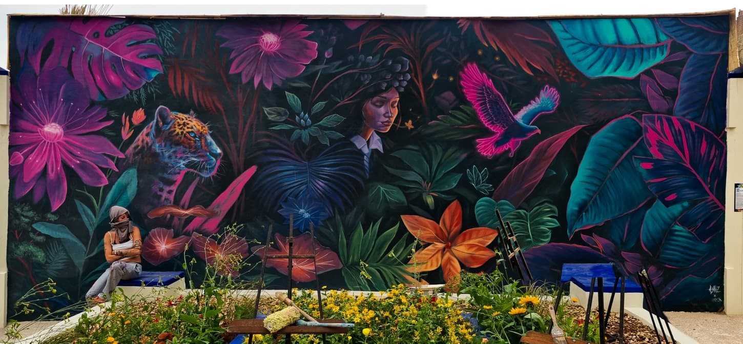 Mural by Alaniz: fluorescent jungle with a jaguar, a woman's face, a pink bird and giant flowers on a long garden wall in Boulogne-sur-Mer